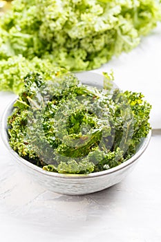 Kale chips in bowl. Crispy green kale chips dehydrated with salt, oil and vegan cheese. Healthy homemade vegan snack