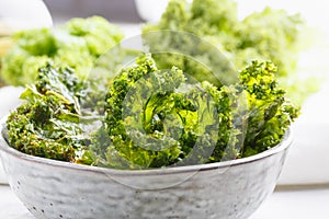 Kale chips in bowl. Crispy green kale chips dehydrated with salt, oil and vegan cheese. Healthy homemade vegan snack