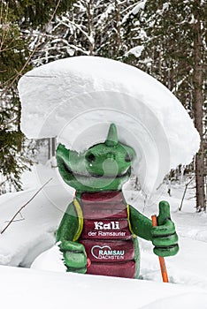 Kali the Ramsaurier, likeable, snow covered, green dinosaur mascot of ski school at ski region Ramsau Dachstein, Steiermark.