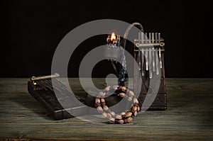 A Kalimba musical instrument made of dark wood with a geometric pattern, a candle holder with a burning candle and an African wome
