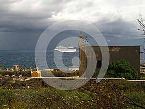 KALKARA, MALTA - Apr 18, 2014: Country side church and cruise-liner approaching the Grand Harbour in Malta, on stormy cloudy day