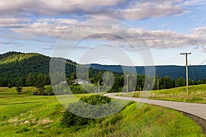 KAMLOOPS, CANADA - JULY 10, 2020: country road through the medow landscape with house on background and cloudy sky