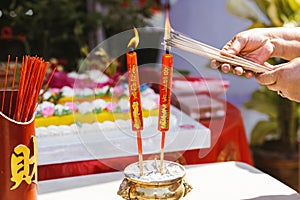 Kamphaeng Phet Thailand-14 Jan 2022: Person hands holds incense stick to light red candle. Worship gods for auspiciousness of life