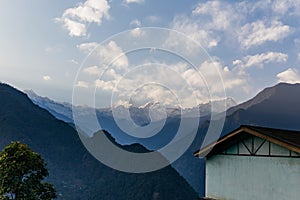 Kangchenjunga mountain with clouds above. Among green hills and house that view in the evening in North Sikkim, India