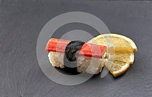 Kani nigiri sushi served with lemon on black slate stone.