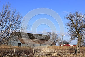 Kansas old Barn on a  Winter day with a Windmill, grass, and blue sky with clouds out in the country.