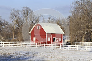 Kansas Red Barn with snow, white fence, tree`s, and a blue sky in Hutchinson Kansas USA.