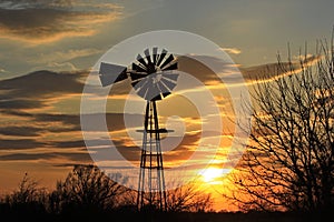 Kansas Windmill Sunset with clouds and a colorful sky with tree`s.