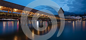 KapellbrÃ¼cke, medieval bridge in Luzern at night. The bridge is illuminated, the lights are reflected in the lake