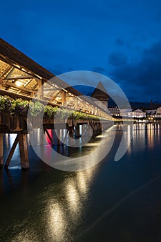 KapellbrÃ¼cke, medieval bridge in Luzern at night. The bridge is illuminated, the lights are reflected in the lake