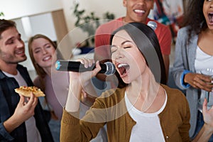Karaoke party. Beautiful young asian girl holding microphone and singing while playing karaoke with best friends at home