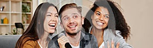 Karaoke singers. Three smiling friends looking happy while playing karaoke at home, singing with microphone, sitting on