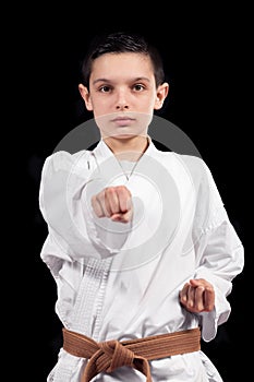 Karate boy in white kimono fighting isolated on black background