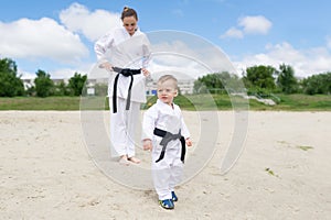 Karate kid - portrait of little boy in the kimono. The boy`s mother is in a kimono at a background.