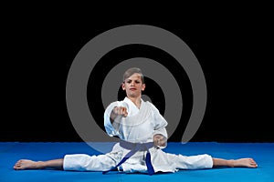 Karate kid wearing white gi and belt in a side split side straddle Chinese split, with arms crossed on