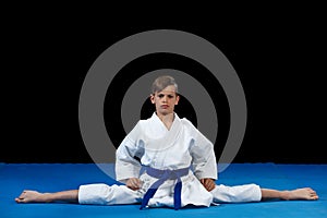 Karate kid wearing white gi and belt in a side split side straddle Chinese split, with arms crossed on