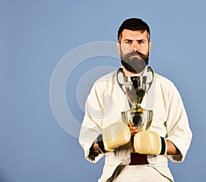 Karate man with serious face in boxing gloves holds cup