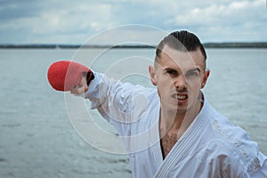 karate man in a sports kimono attacks with his hand. the face is aggressive, screaming something. face out of focus.