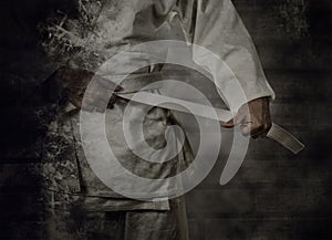 Karateka tying the white belt (obi) with grunge background photo
