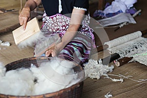 Karen woman brushing wool yarn with special brush.