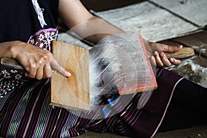 Karen woman brushing wool yarn with special brush.