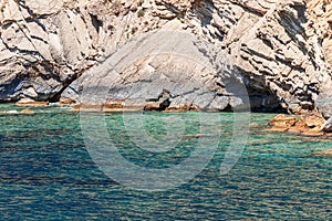 Karst rocks of the coastal shore of Ibiza island, whitened by the constant sun and sea, and the green-blue waters of bay photo
