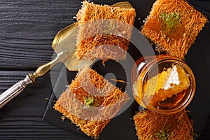 Kataif cake with pistachios and fresh honey close-up on a table.