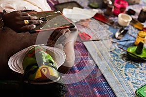 Katakhali dance performer doing face paint and makeup in front of hand held mirror