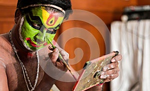 Katakhali dance performer doing face paint and makeup in front of hand held mirror