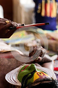 Katakhali dance performer doing face paint and makeup in front of hand held mirror