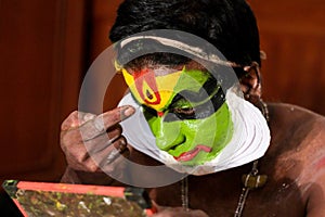 Katakhali dance performer doing face paint and makeup in front of hand held mirror