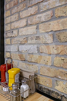 Katchup, Mustard, salt, pepper and napkins next to a brick wall