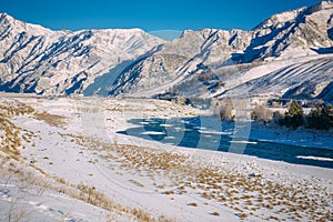 The Katun river flows through a snow-covered valley. Winter landscape of mountain peaks and blue sky. Travel to the Altai