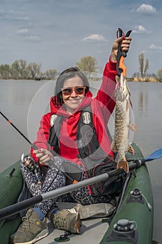 Kayak fishing. Fisher girl holding pike fish trophy on inflatable boat with fishing tackle at lake