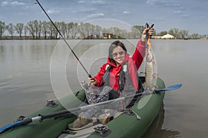 Kayak fishing. Fisher girl holding pike fish trophy on inflatable boat with fishing tackle at lake