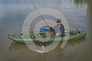 Kayak fishing. Fisherman caught pike fish on inflatable boat with fishing tackle at lake