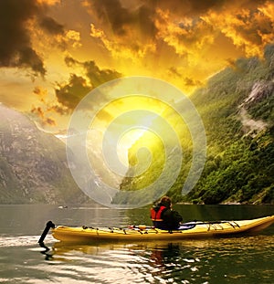 Kayaker eaves Geiranger fjord bay at rainy day in Norway