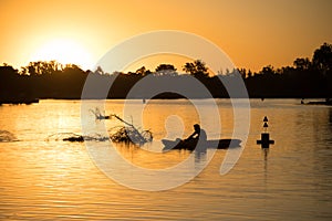 Kayaker silhouette at sunset on a river with floating logs and branches. Outdoor water sports