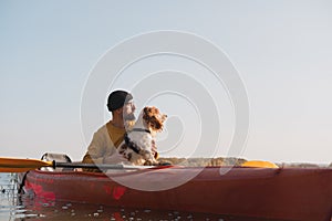 Kayaking with dogs: man sits in a row boat on the lake next to his spaniel.