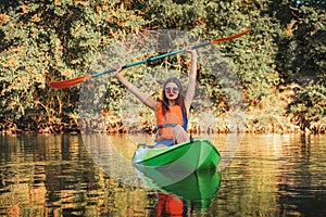 Kayaking on the river. A young tanned woman in a life jacket is sitting in a kayak with an oar raised up