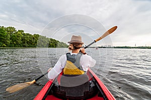 Kayaking travel. Young lady paddling the red kayak. Back view. Holiday and summer adventure