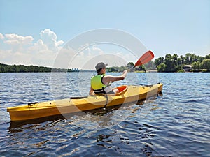 Kayaking A young boy is sailing a canoe on a wide river. Rear view. Sports tourism and active leisure in beautiful summer nature