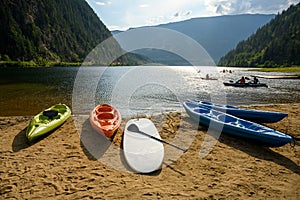 Kayaks, canoes, and other recreational watercrafts lying on the sandy beach while some people are kayaking, canoeing on the Three
