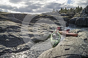 Kayaks stand moored on a rocky shore, in the background there is