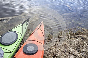 Kayaks stand moored on the shore of the lake.