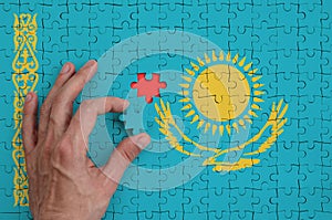 Kazakhstan flag is depicted on a puzzle, which the man`s hand completes to fold