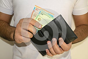 Kazakhstan national currency. KZ money banknotes. Man in white t-shirt put tenge banknotes into a black wallet.