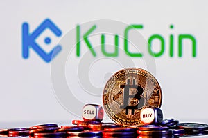 Golden bitcoin with two buy-sell cubes in a pile of coins on the background of the KuCoin logo. The concept of buy-sell choice