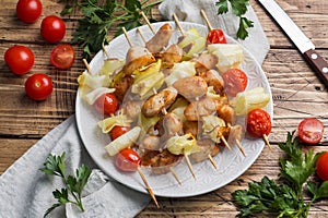 Kebab chicken, zucchini and tomatoes on skewers in a plate. Wooden table