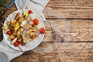 Kebab chicken, zucchini and tomatoes on skewers in a plate. Wooden table. Copy space